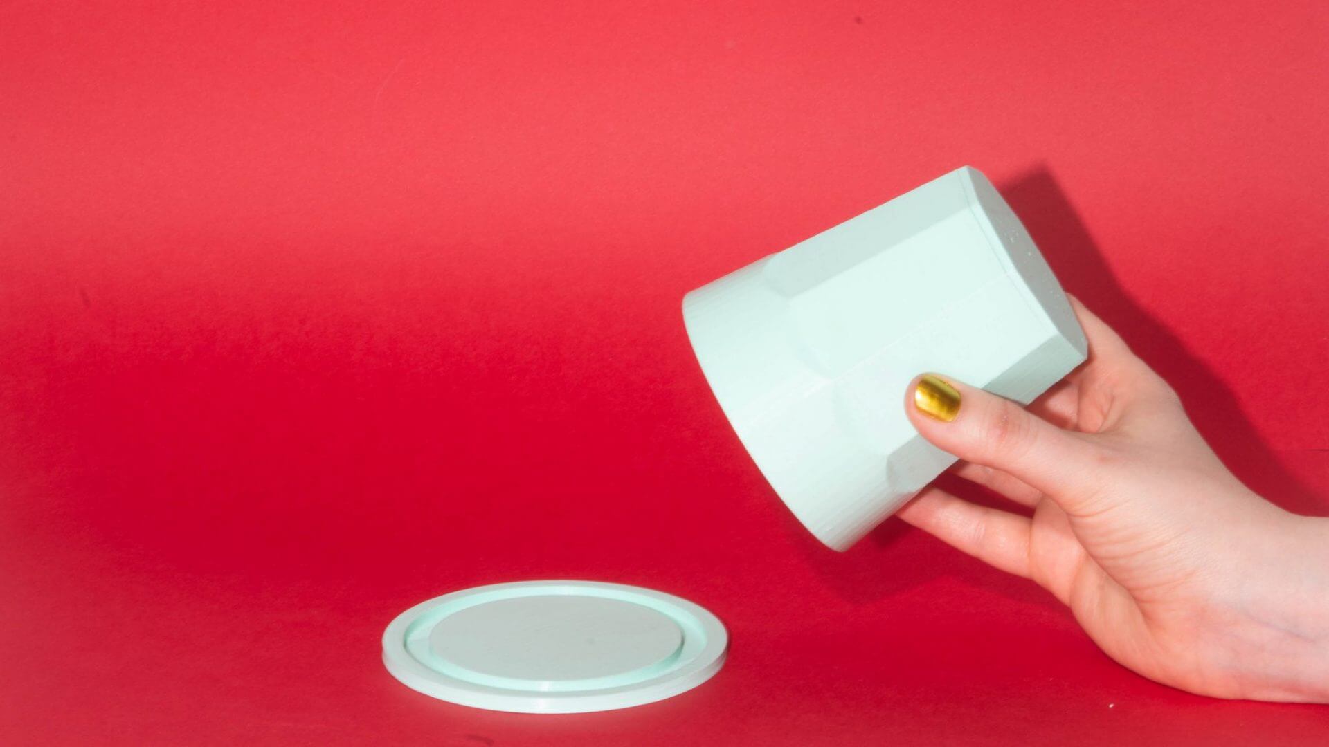 A hand grabbing a mint coloured cup in front of a red background